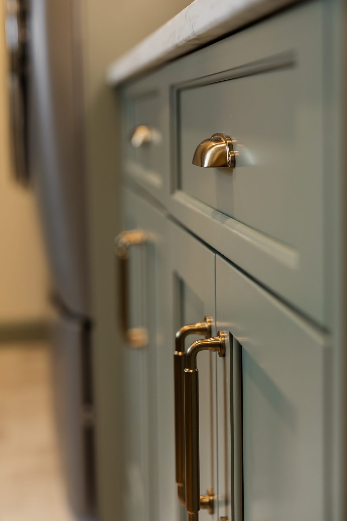 Sage green cabinetry with brass hardware and marble counter