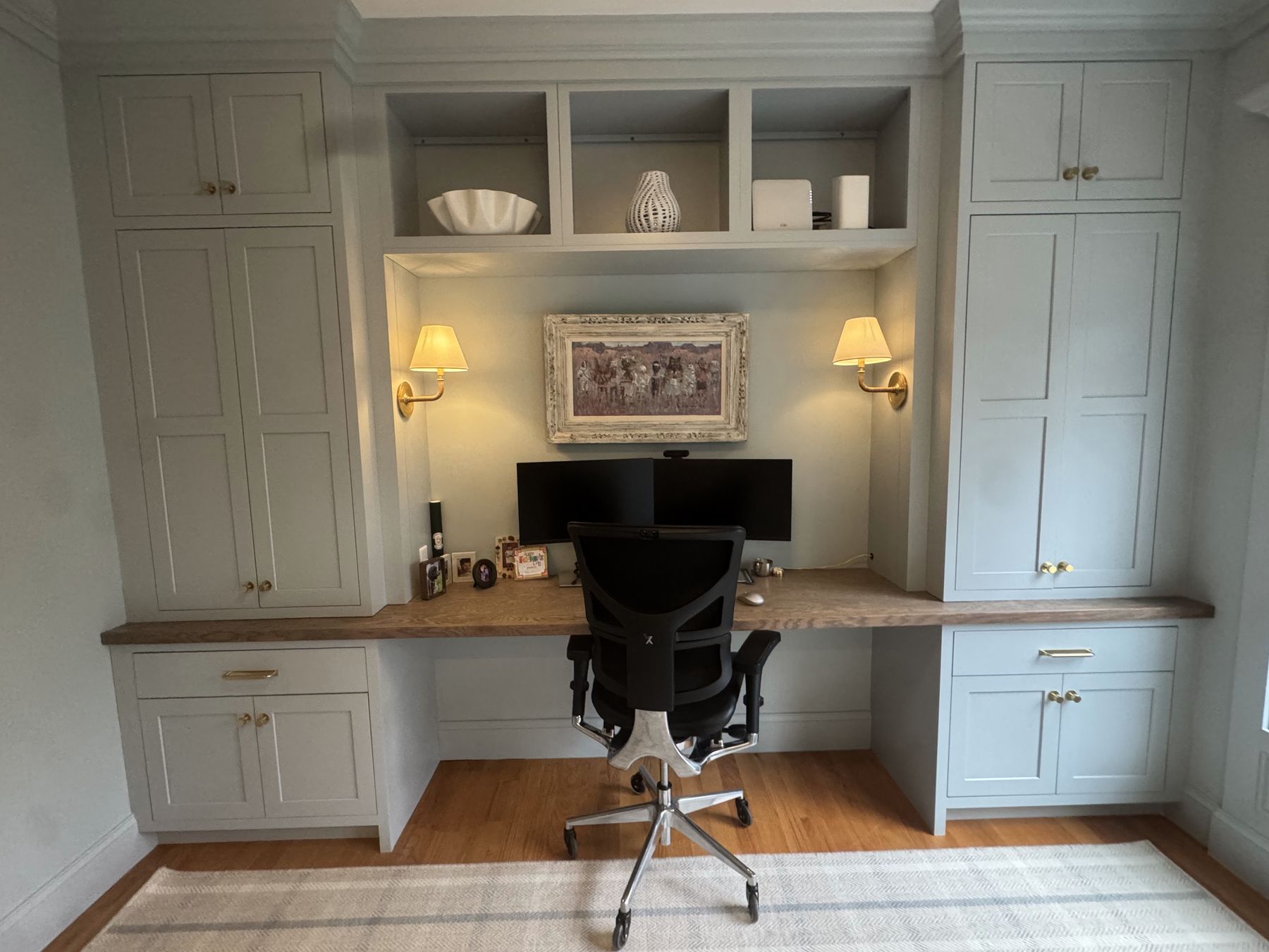 Home office with sage green built-ins, wood desk, brass sconces and hardware